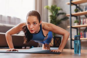 mulher praticando exercícios físicos em casa com colchonete e halteres