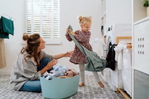 menina feliz ajudando mulher mãe a retirar as roupas limpas da máquina de lavar