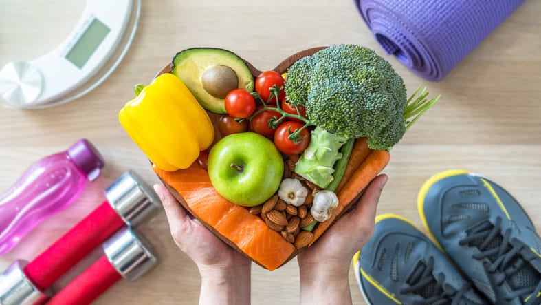pessoa segura nas mãos bandeja em formato de coração com frutas, legumes e verduras saudáveis