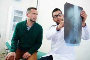 homem em consulta médica olhando para raio-x da coluna vertebral com médico apontando para a imagem
