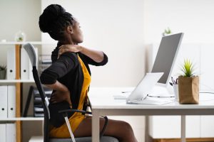 mulher jovem sentada em escritório em frente ao notebook com sentindo dor nas costas ou na coluna