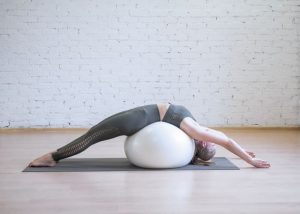 mulher realizando posição de pilates que estende a coluna vertebral com bola de pilates no chão